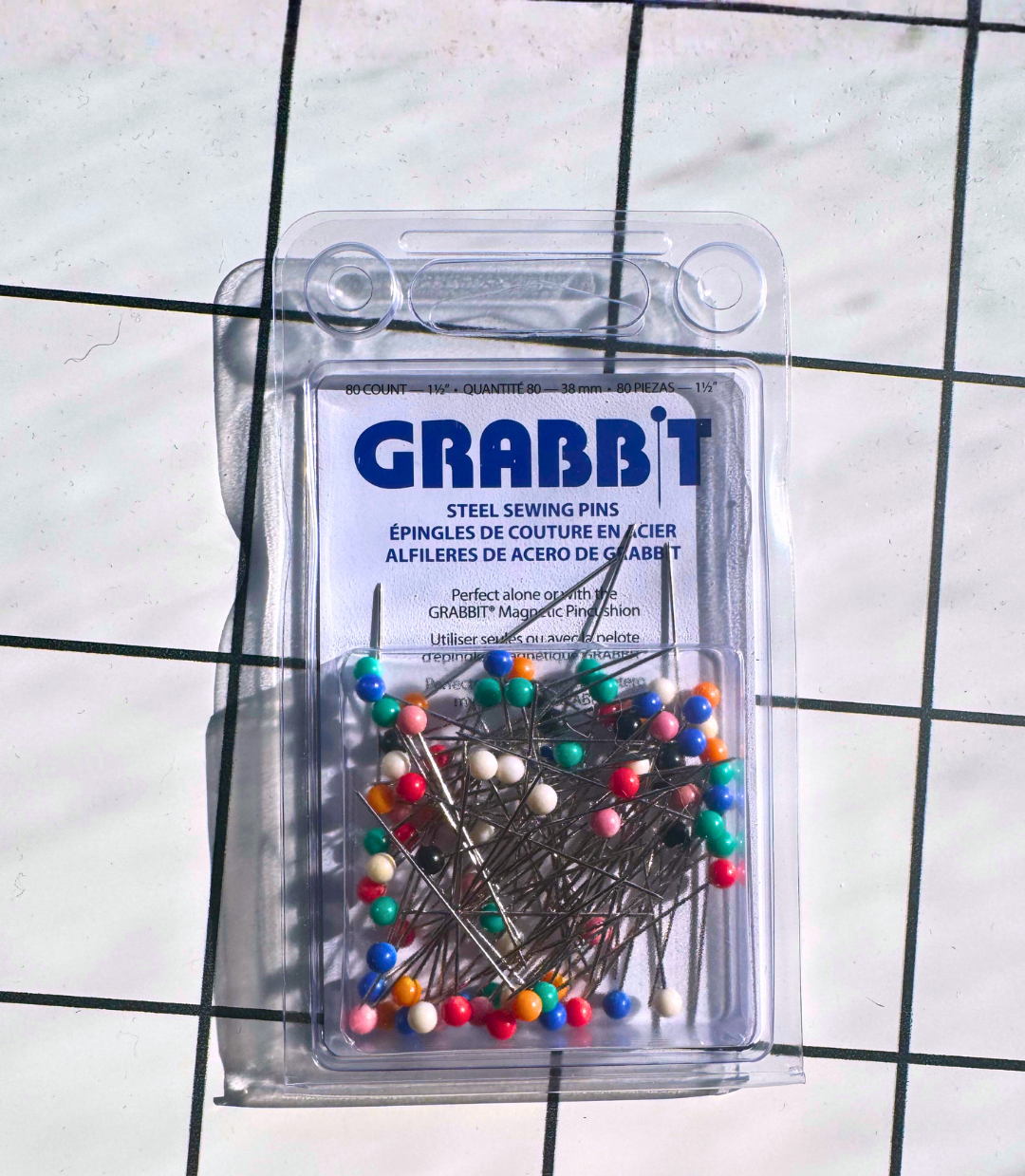 Packaged colorful sewing pins with 'GRABB'T' branding on a grid background
