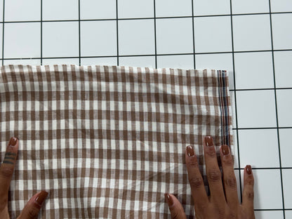 Brown and white checkered fabric held by hands on a grid background