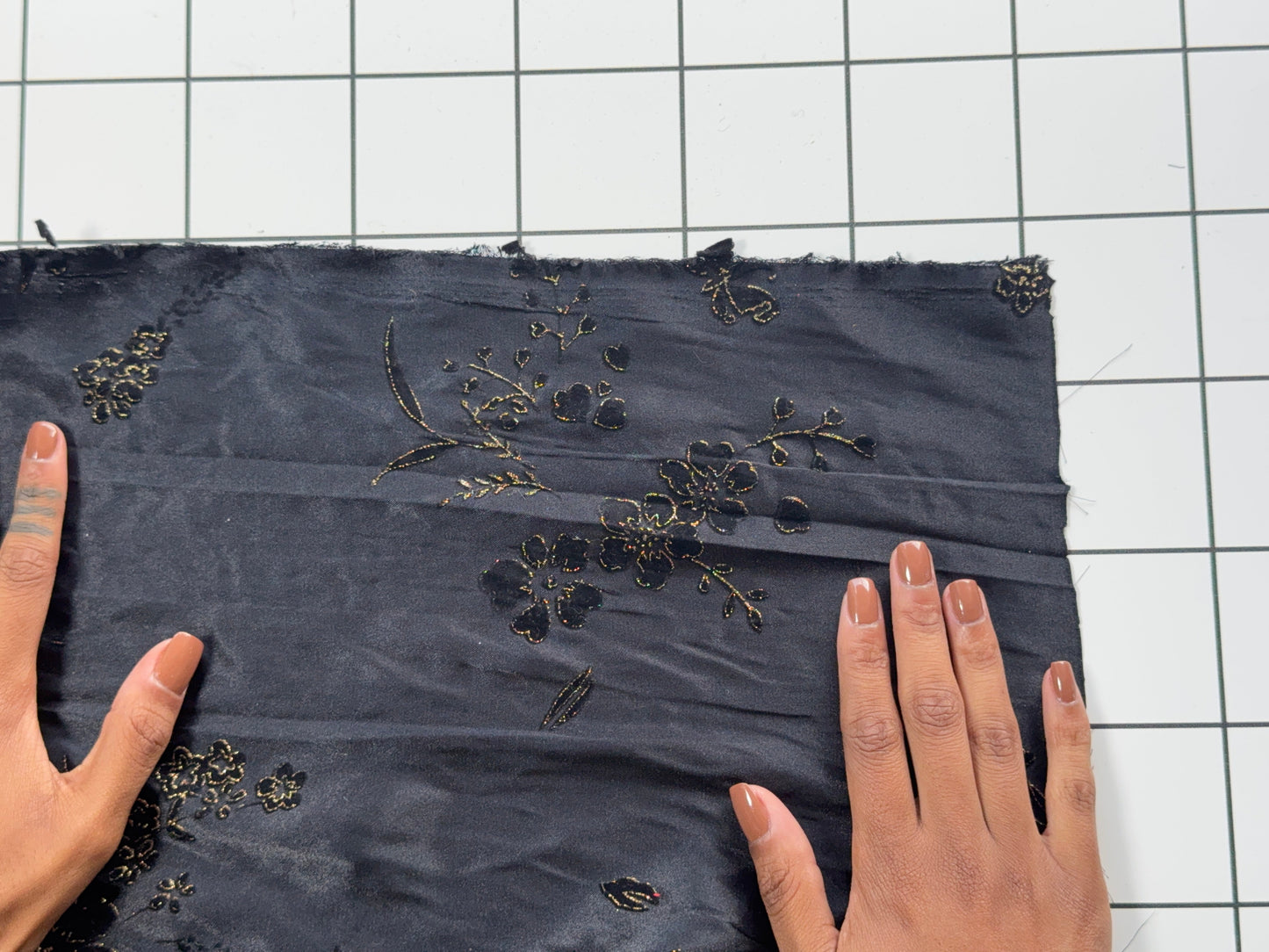Black fabric with floral embroidery held by hands on a grid background