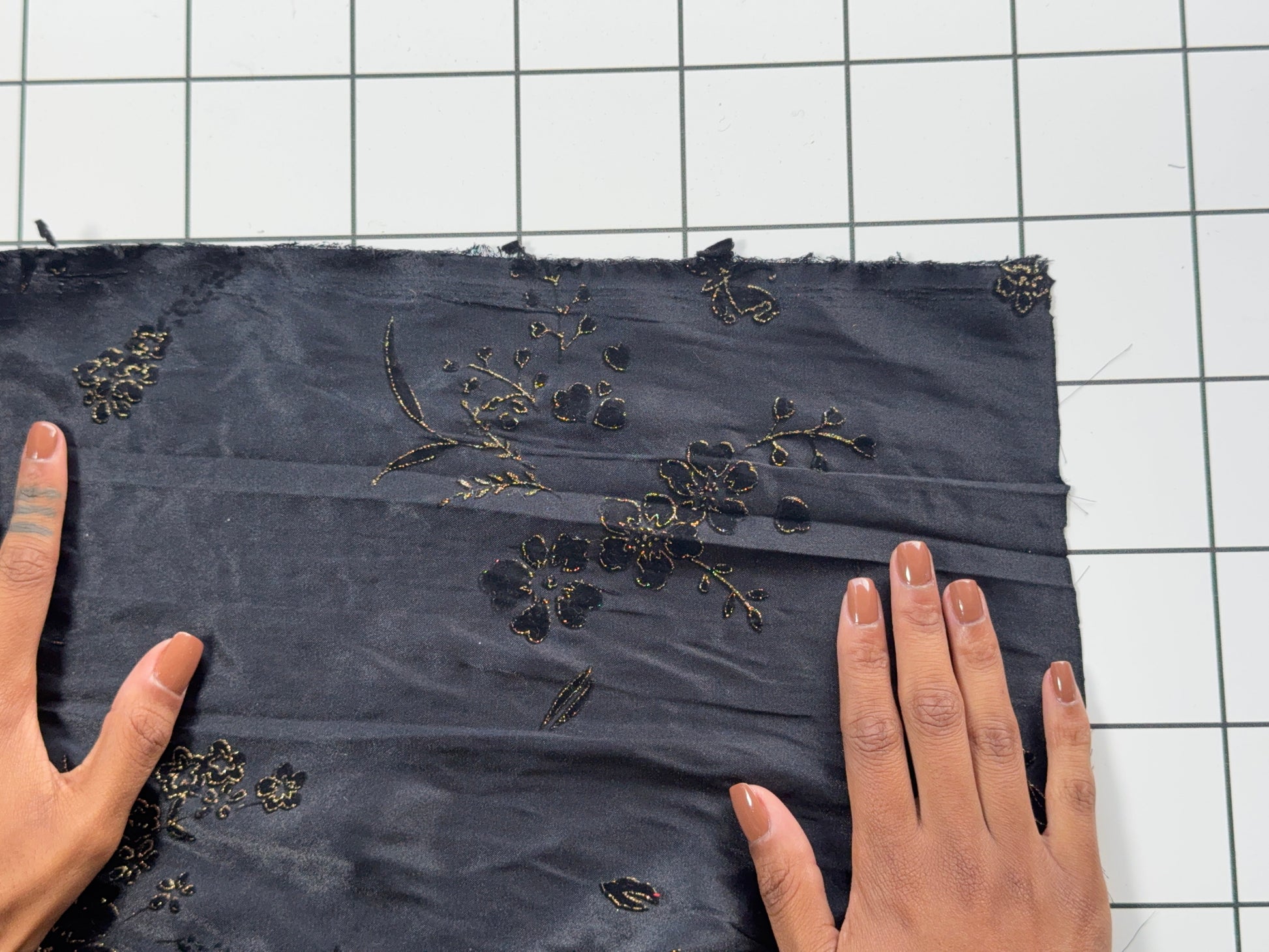 Black fabric with floral embroidery held by hands on a grid background