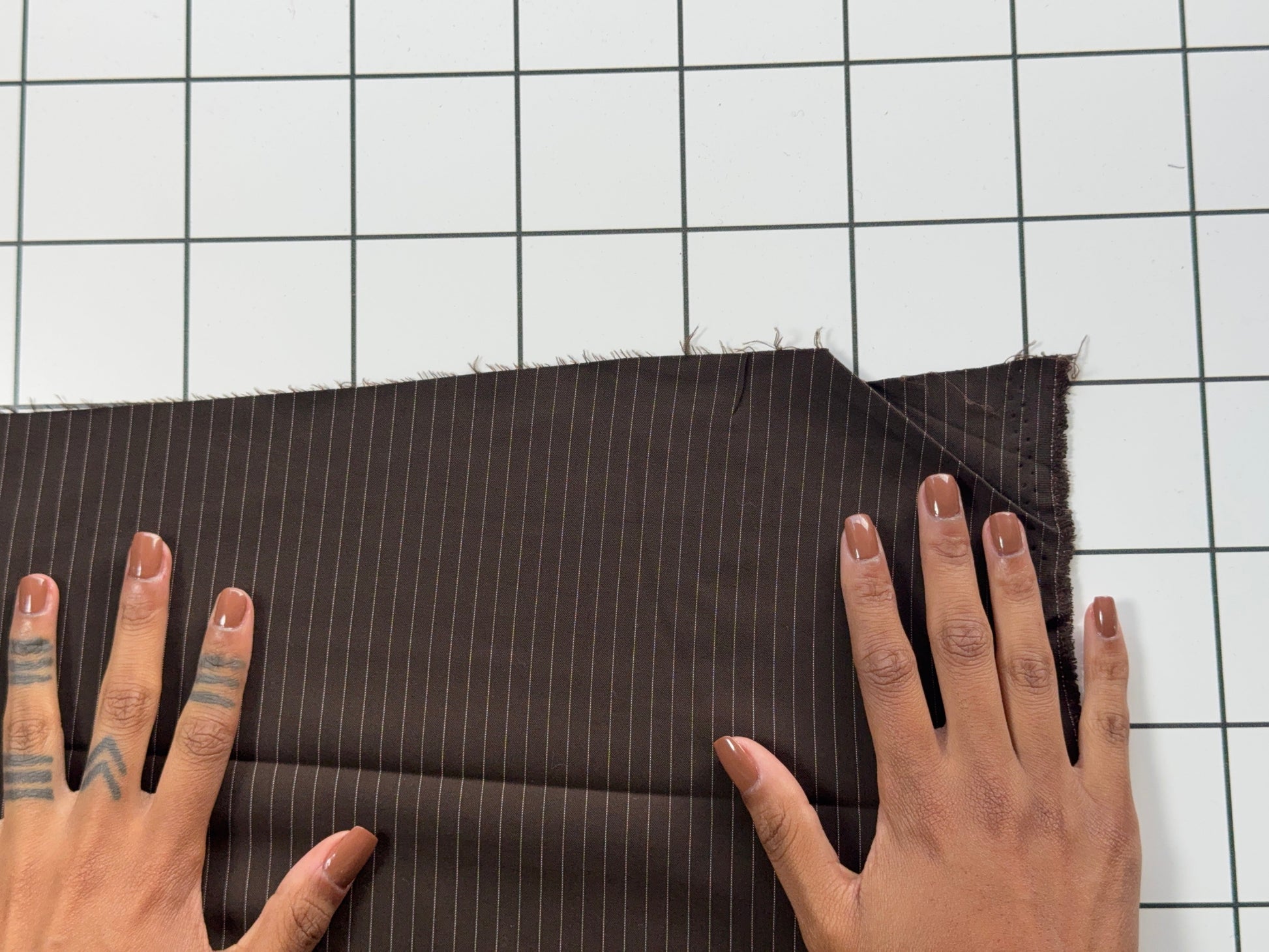 Brown pinstripe fabric being held by hands on a grid background